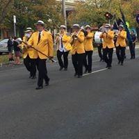Maffra Municipal Band playing as they are marching down a street with their band leader at the helm