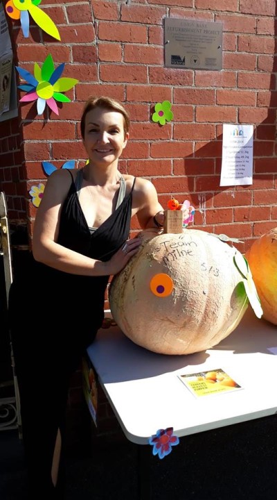 Outside entrance of Yarram Neighbourhood House with girl standing next to display table with large competition sized pumpkins on it.  